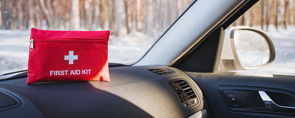 A first aid kit atop of the dashboard of a car, in a winter setting.