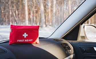 A first aid kit atop of the dashboard of a car, in a winter setting.