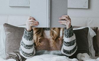 A woman in bed, reading a book.