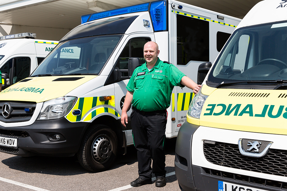 Male ambulance driver in St John uniform standing in front of an ambulance with St John Ambulance ambulance