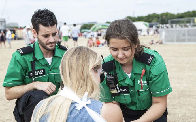 Two SJA first aiders help a patient with her arm in a sling at event Two SJA first aiders help a patient with her arm in a sling at event