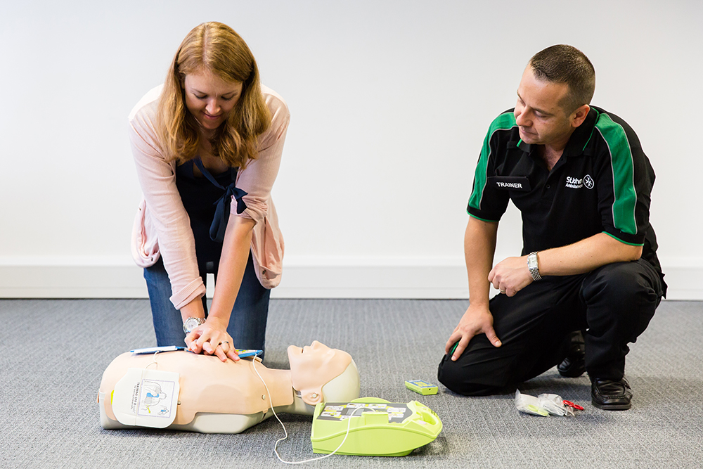 St John Ambulance trainer teaching woman to perform CPR on a training manikin.