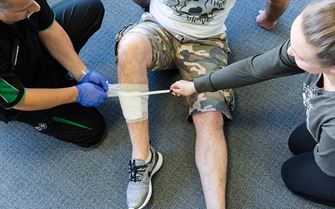 Trainer demonstrates how to apply a bandage to a leg wound during a first aid course. Trainer demonstrates how to apply a bandage to a leg wound during a first aid course.