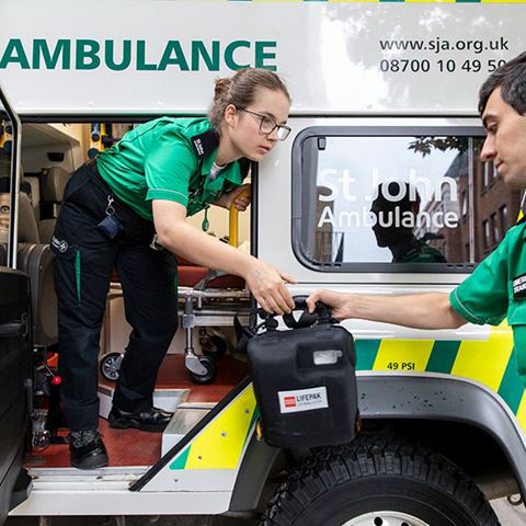 A volunteer standing in an ambulance passing a defibrillator to another volunteer. A volunteer standing in an ambulance passing a defibrillator to another volunteer.