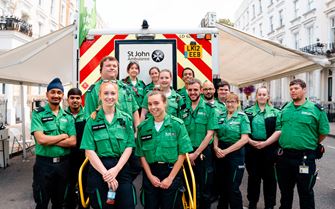 A group of 15 St John Ambulance first aider volunteers standing in front of an ambulance. A group of 15 St John Ambulance first aider volunteers standing in front of an ambulance.