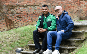 A young man in St John Ambulance uniform sitting with an older man, both smiling