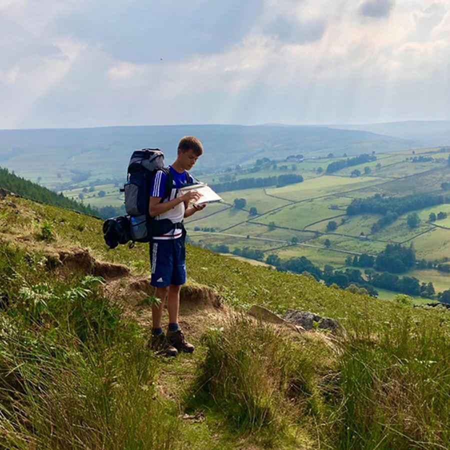 Duke of Edinburgh expedition participant looking at a map surrounded by countryside.