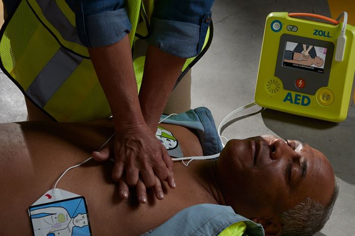 A man using a ZOLL defibrillator on a patient.